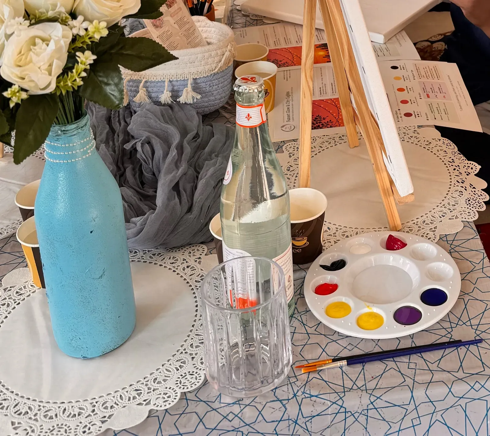 Painting station with a palette in warm sunset colours, a brush, a glass of water and white roses
